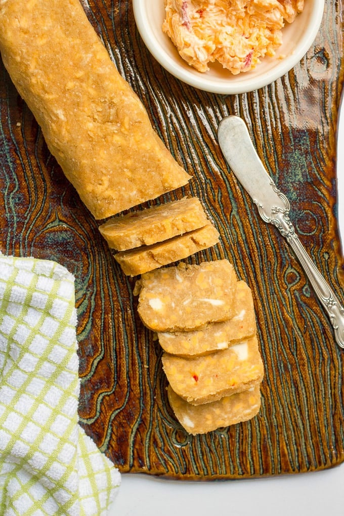 A rolled and sliced log of dough for making cheese crackers on a textured board.