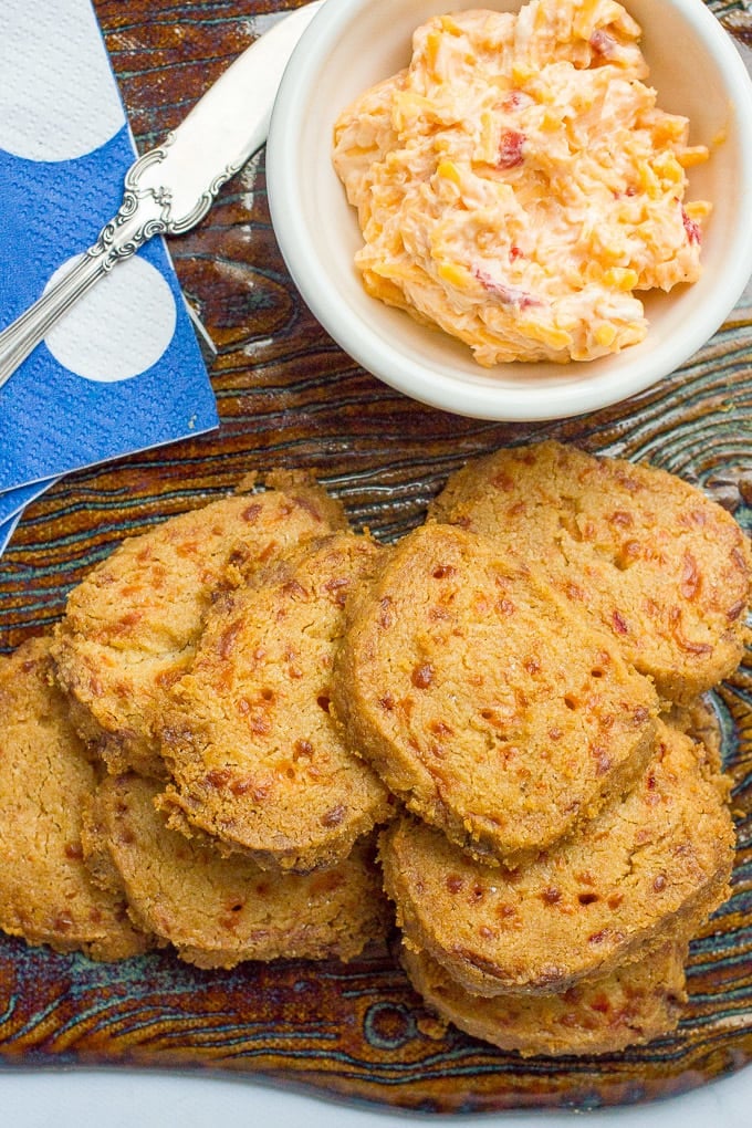 A stack of pimiento cheese crackers on a serving tray with a bowl of pimiento cheese to the side.