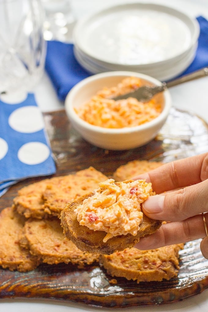 A hand holding up a homemade cheese cracker with a smear of pimiento cheese on top.