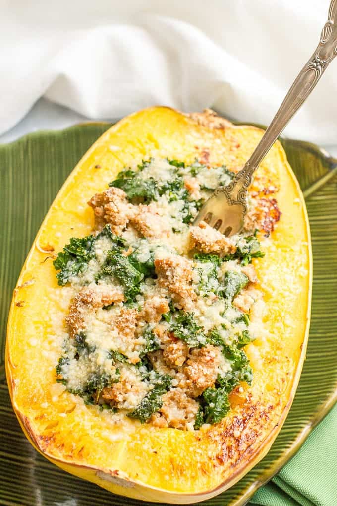 A fork resting in a halved roasted spaghetti squash stuffed with a turkey sausage and kale mixture and topped with Parmesan cheese.