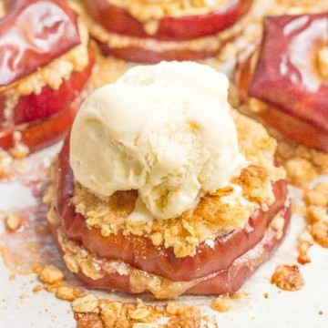 Close up of baked sliced apples layered with streusel and stacked on a parchment paper lined baking sheet with a scoop of ice cream on top.