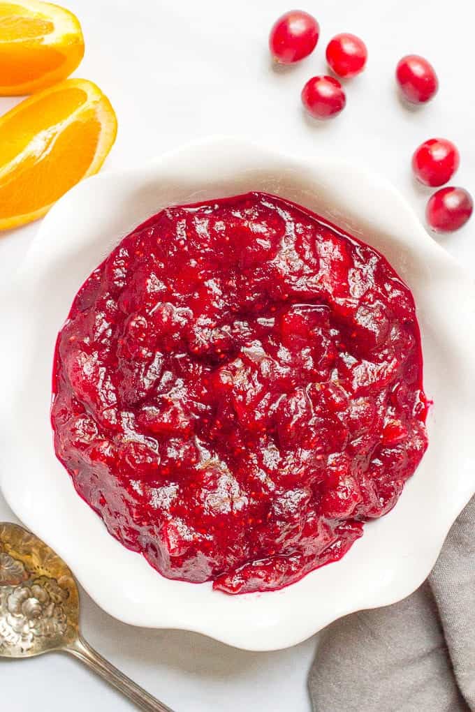 A homemade easy cranberry sauce in a white serving bowl with cranberries scattered nearby