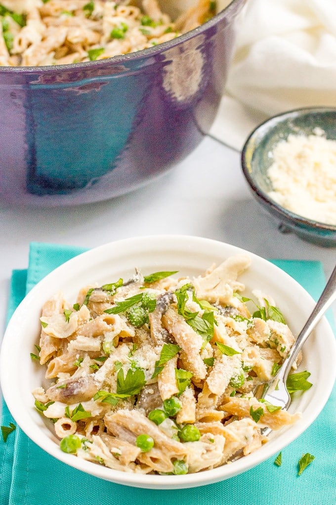 A bowl of pasta with chicken and mushrooms with parsley on top served with a fork