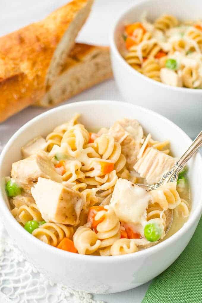 A spoon resting in a bowl with a serving of a turkey noodle soup with vegetables and shredded cheese.
