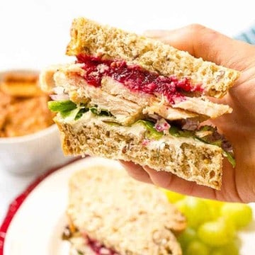 A hand holding up a sandwich with leftover Thanksgiving turkey, cranberry sauce and spinach.