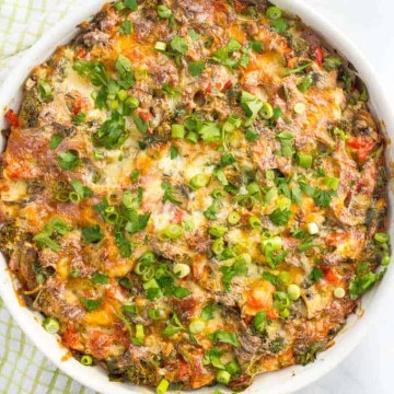A baked breakfast casserole with turkey sausage and vegetables in a large round white baking dish with sliced green onions sprinkled on top.