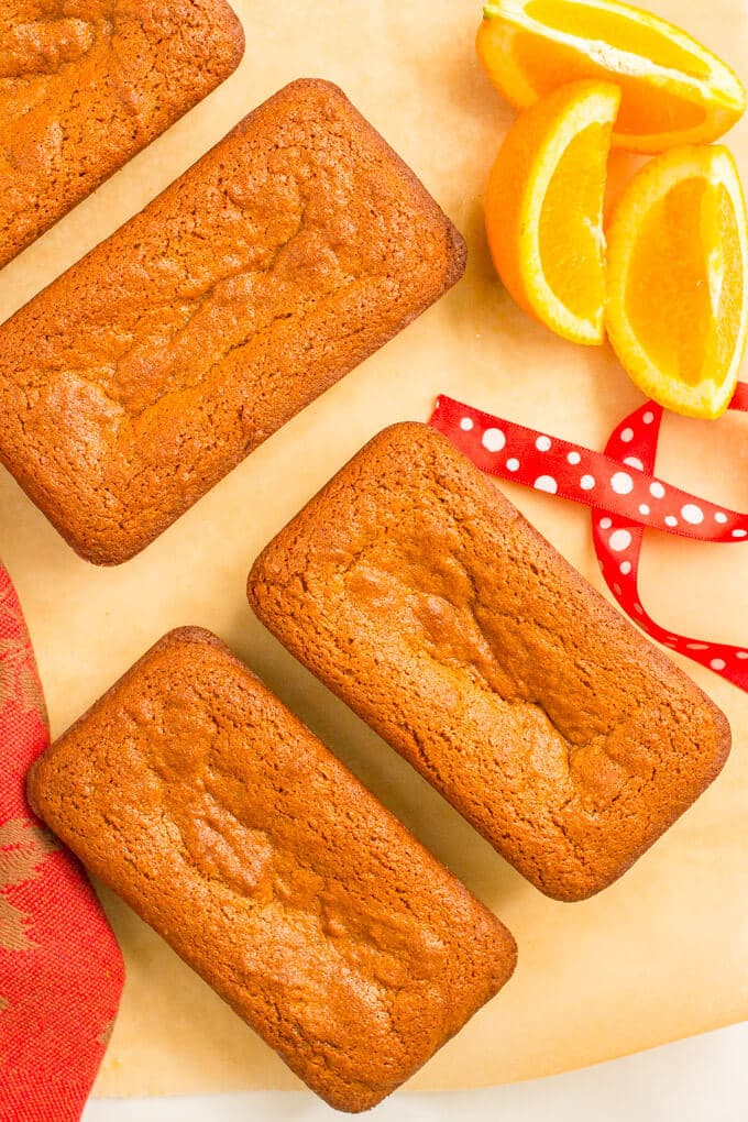 Mini whole wheat gingerbread loaves scattered on parchment paper with orange slices nearby