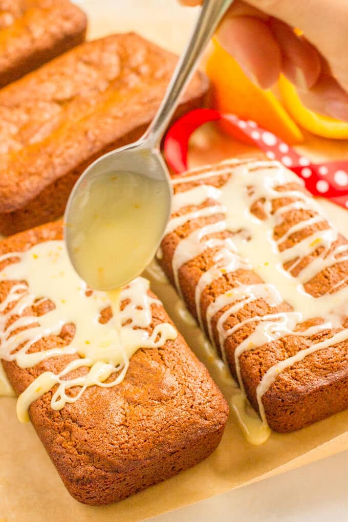 A drizzle of orange glaze being added to a small gingerbread loaf