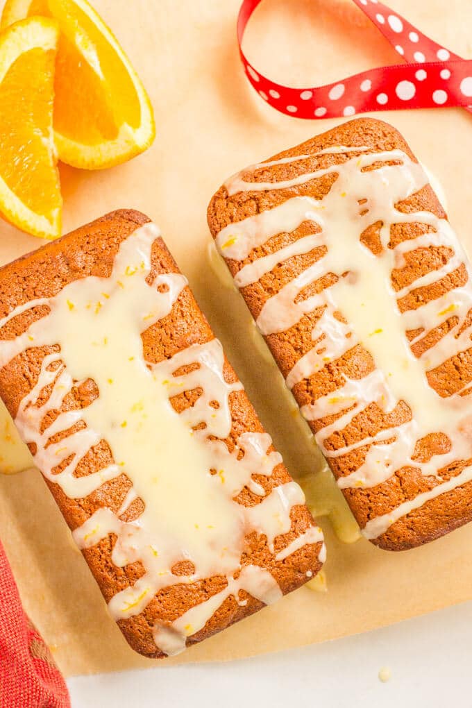 Small mini loaves of gingerbread with an orange glaze drizzled on top and orange slices nearby