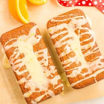 Two small gingerbread loaves topped with orange icing with orange slices nearby.