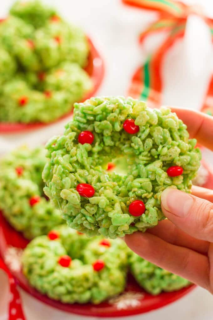 A hand holding a green Rice Krispie wreath with red hots