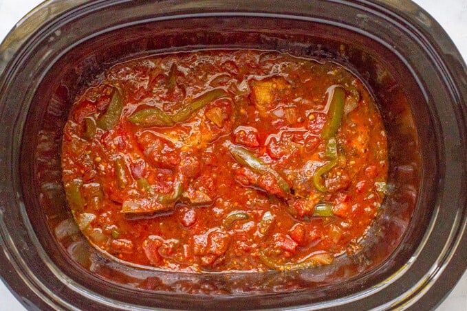 A slow cooker with pork chops and an Italian tomato sauce