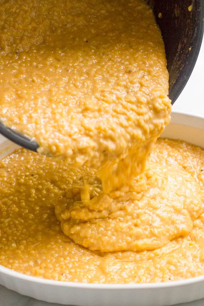 Cheesy grits being poured into a casserole dish