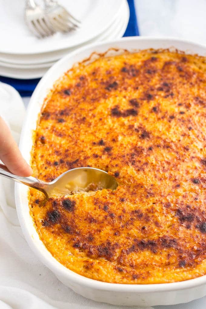 Overnight cheesy grits casserole with a spoon getting ready to serve it