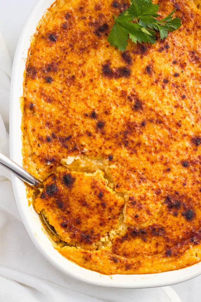 A scoop being taken out of a cheesy grits casserole