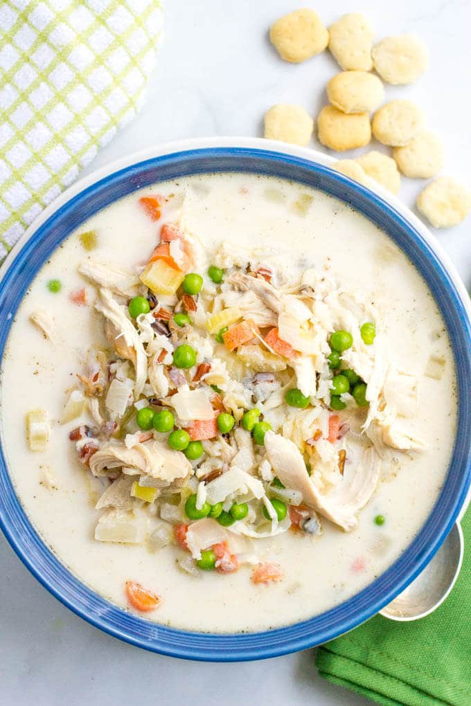 A creamy chicken soup with veggies served in a blue bowl with soup crackers scattered to the side.