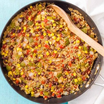 A large dark skillet with quinoa, black beans, corn and peppers mixed and cooked together.