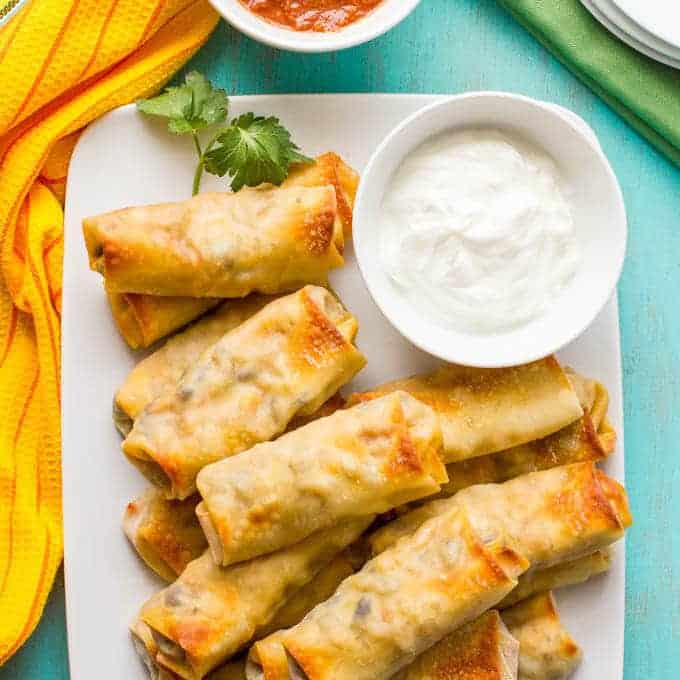 Baked browned egg rolls arranged on a serving platter with a bowl of sour cream for dipping