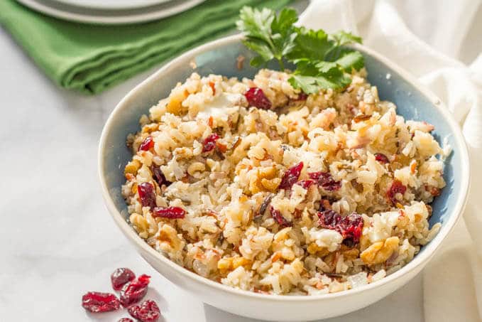 Wild rice salad with dried cranberries served in a white and blue bowl with a sprig of parsley tucked in