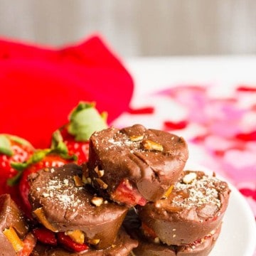 A stack of fudge cups with bits of strawberries and pretzels mixed in on a small white plate with fresh strawberries to the side.