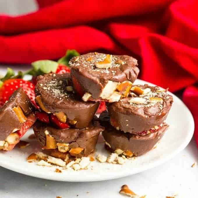 A stack of mini chocolate fudge cups with pretzels and strawberries on a white plate