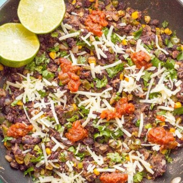 A skillet full of a deconstructed veggie burger mixture topped with salsa, shredded cheese, cilantro and a halved lime to the side.
