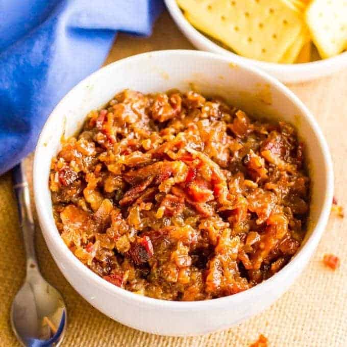 Bourbon bacon jam in a white bowl with crumbled bacon scattered around the bowl