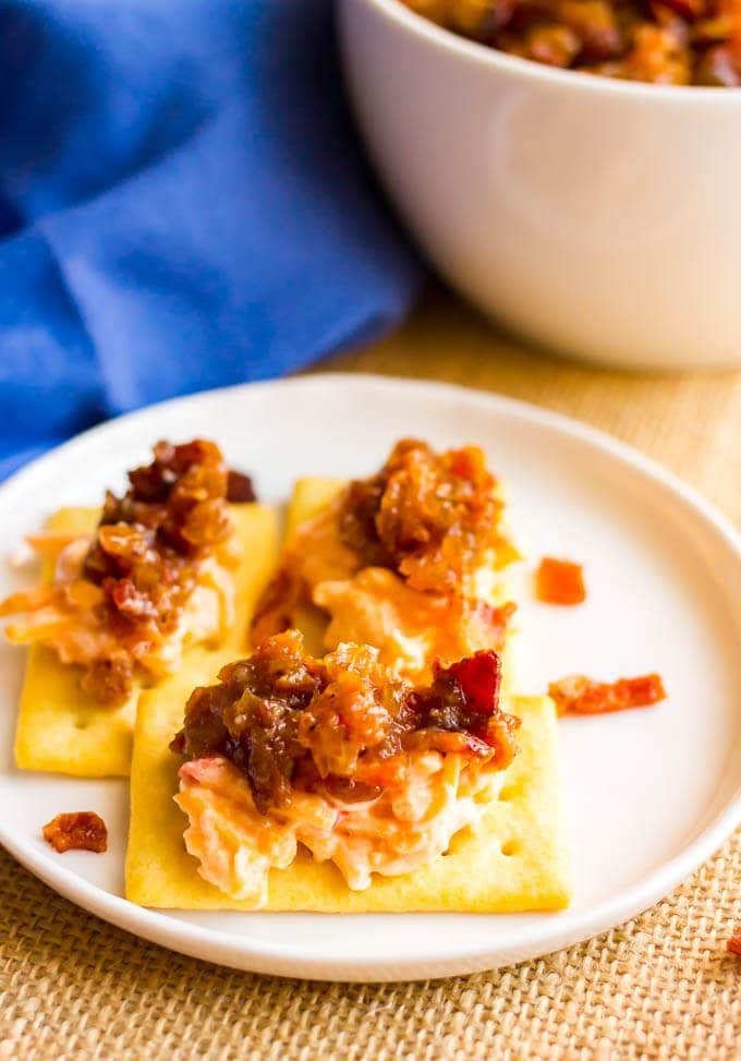 Crackers with pimiento cheese and bacon jam on top served on a small white plate