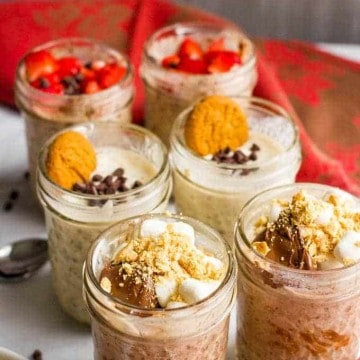 Six small glass jars each with a chocolate overnight oats mixture topped with a variety of different toppings, including chopped strawberries, mini chocolate chips and a smores mixture.