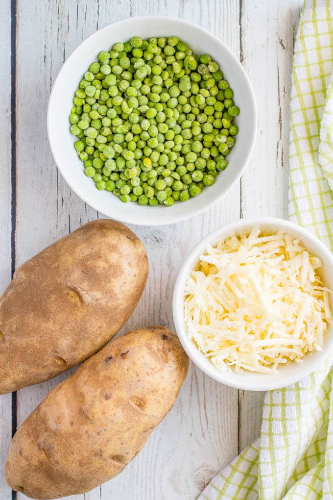 Potatoes, shredded cheese and green peas in a bowl laid out on a table