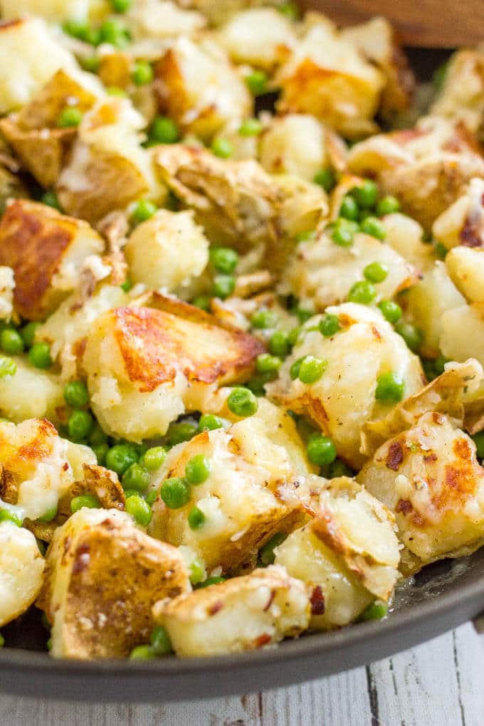 Close up of cheesy potatoes and peas in a large skillet