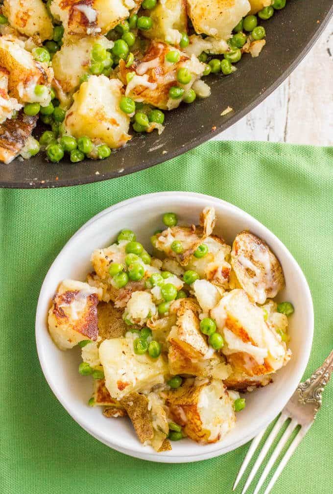 A serving of cheesy potatoes and peas served in a small white bowl with a fork nearby