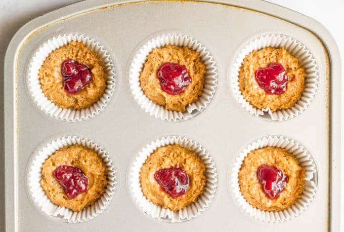 Peanut butter muffin batter in a muffin tin with dollops of jelly in the middle