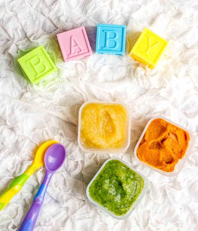 A trio of different colored baby food purees with baby spoons and blocks spelling out b-a-b-y