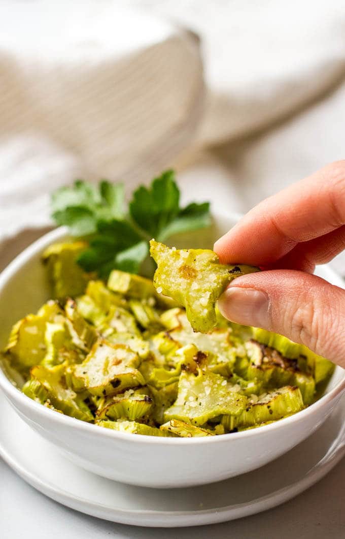 A hand picking up a small slice of a roasted broccoli stalk