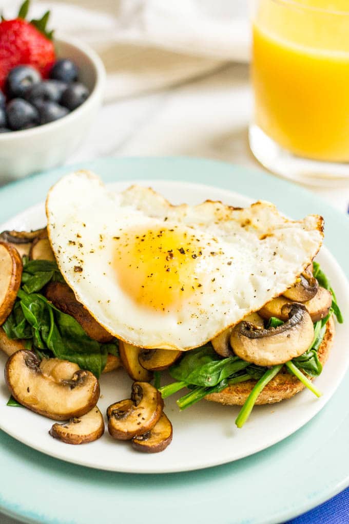 A toasted whole wheat bagel topped with sautéed mushrooms and spinach with a fried egg on top