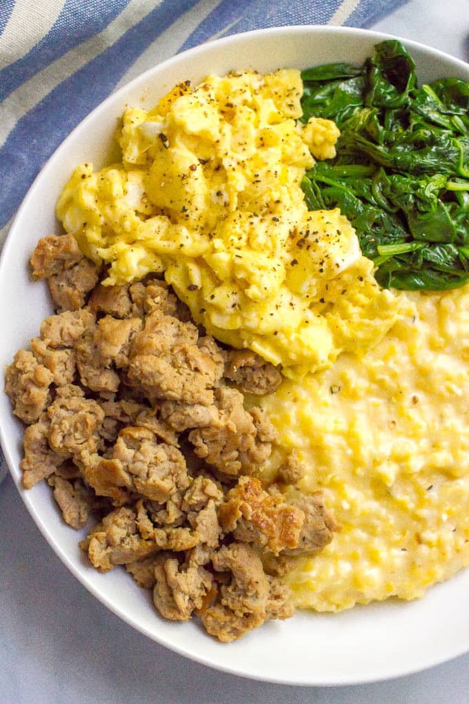 A breakfast bowl of cheesy grits with crumbled sausage, scrambled eggs and sautéed spinach