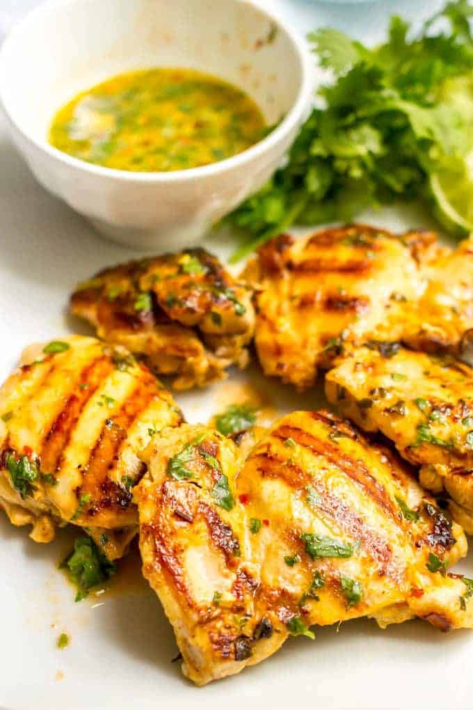 Grilled chicken thighs on a white plate with a small bowl of marinade in the background.