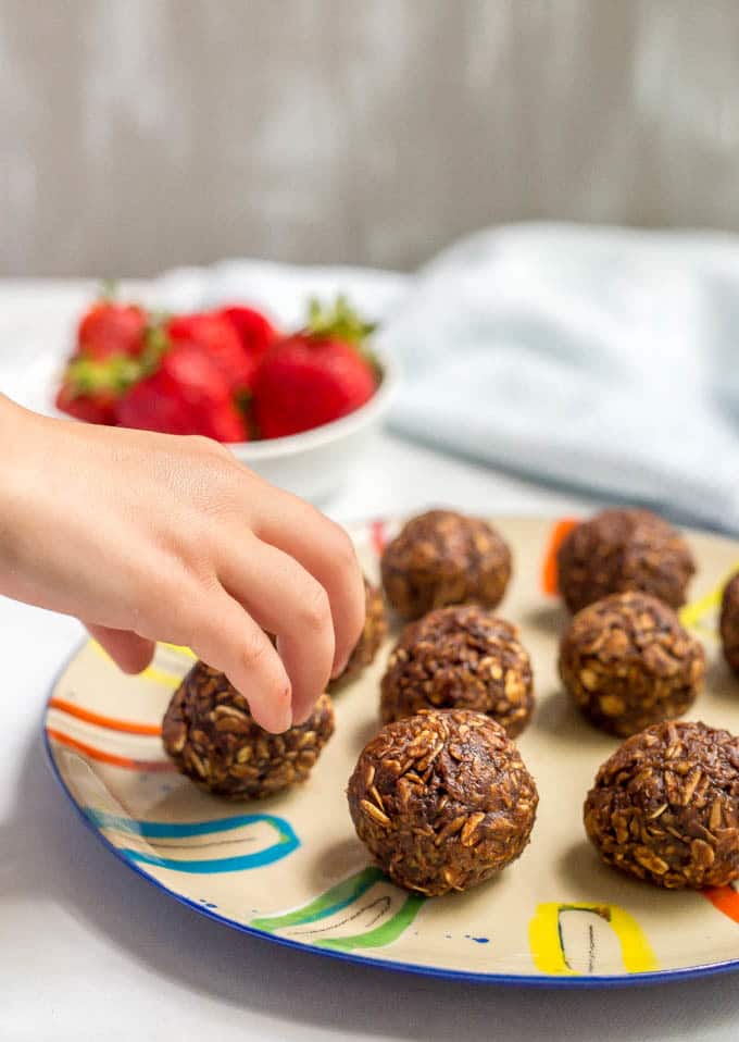 Chocolate cookie balls arranged on a plate with a hand reaching for one.