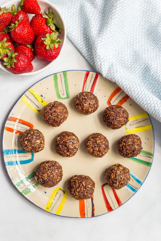 Chocolate cookie balls overhead shot on colorful plate with bowl of strawberries beside