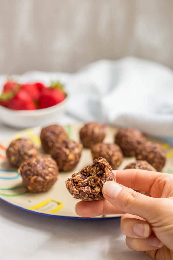 A hand holding a chocolate oat cookie ball that's had a bite taken out of it.