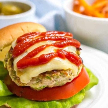 A turkey burger with shredded zucchini in the patty served on a bun with lettuce and tomato and topped with melted cheese and ketchup.