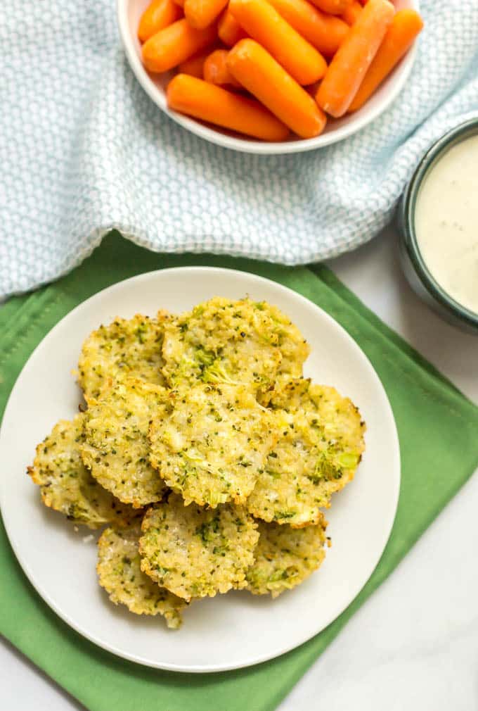 Overhead shot of cheesy broccoli quinoa bites on a white plate with a bowl of carrots and a bowl of Ranch dressing to the side.