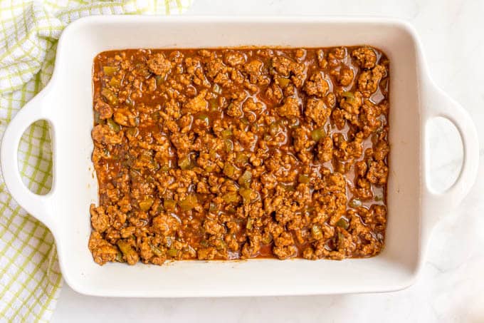 Cheesy sloppy Joe casserole being assembled with sloppy Joe mixture in the casserole dish