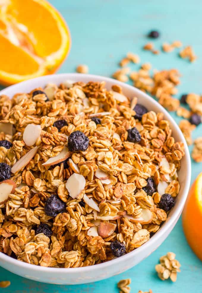 A bowl full of granola with blueberries and almonds and oranges nearby