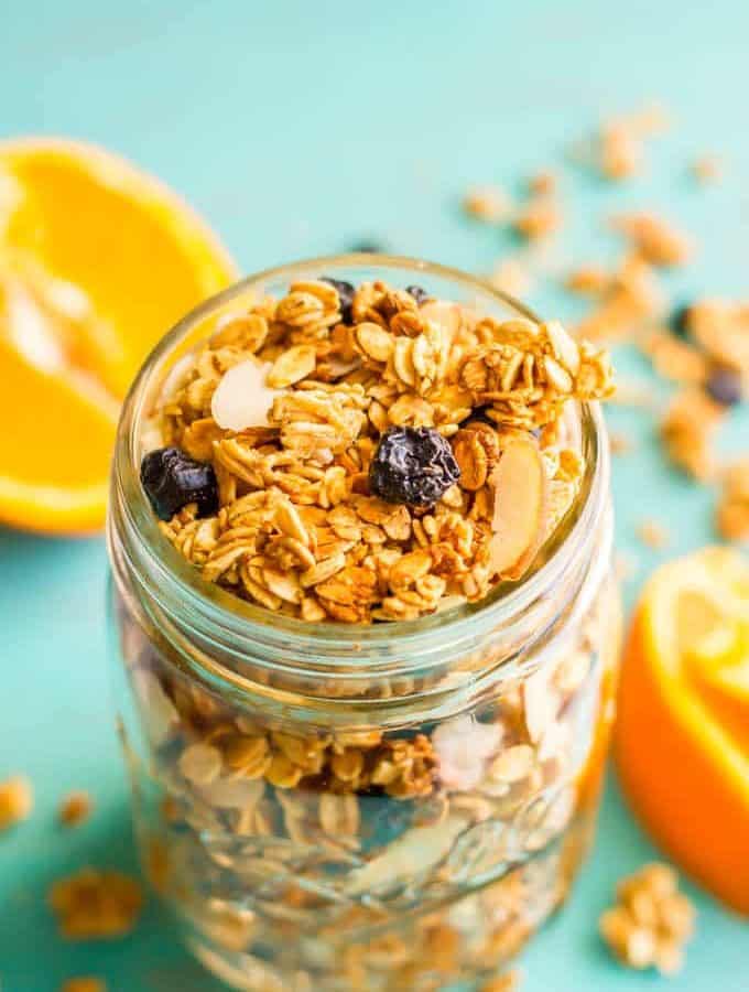 A glass jar full of a homemade citrus granola with dried blueberries and slivered almonds mixed in.
