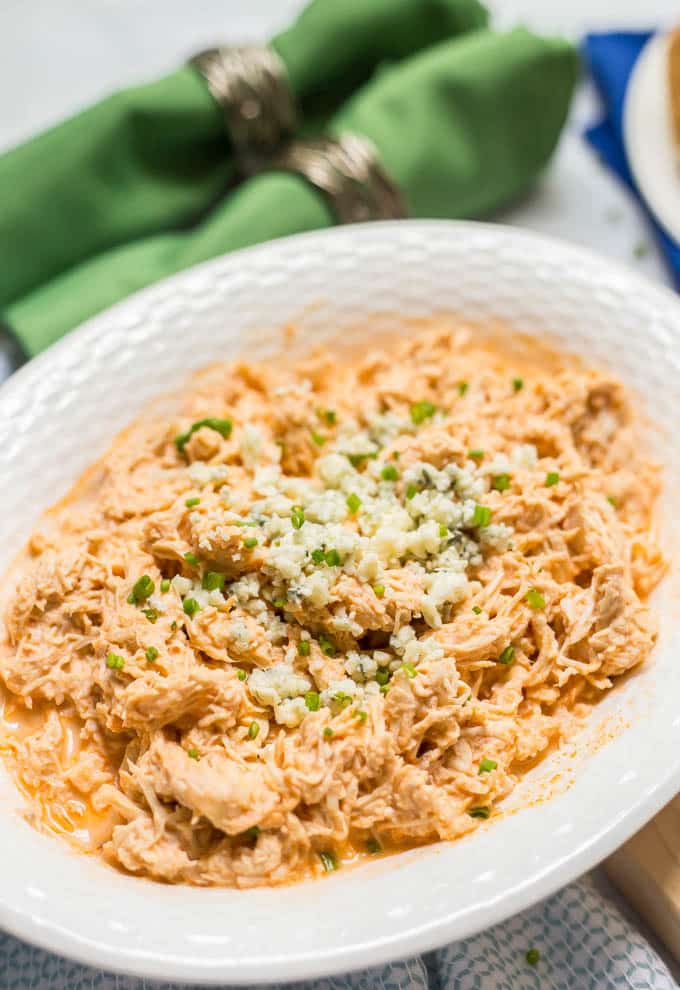 A white serving bowl filled with buffalo chicken topped with blue cheese and chives