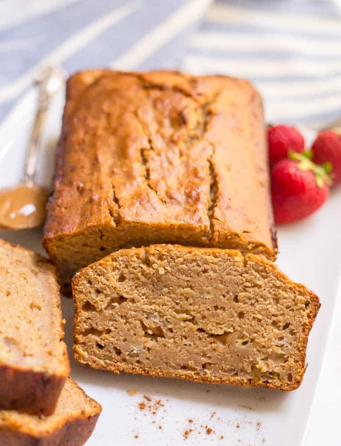 Whole wheat peanut butter banana bread sliced on plate with strawberries and a spoonful of peanut butter