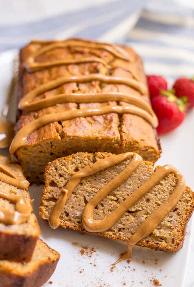 Sliced peanut butter banana bread served on a white platter with a drizzle of peanut butter over the slices and the rest of the loaf.