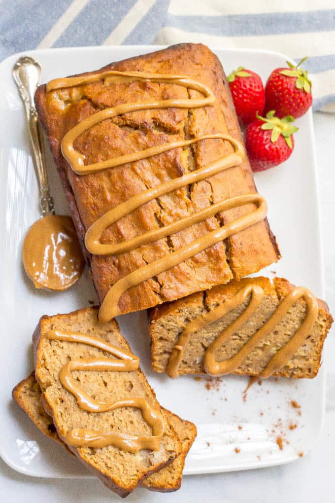 Close up of a peanut butter banana bread served on a white platter with a few slices cut and a drizzle of peanut butter over the whole thing.